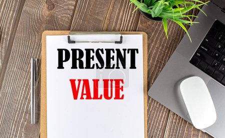 PRESENT VALUE text on a paper clipboard with laptop and mouse on wooden background , business concept