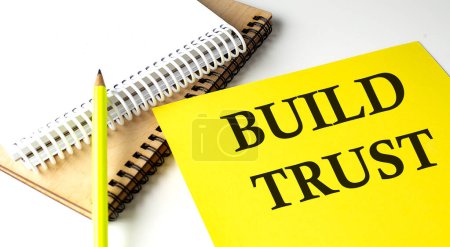 BUILD TRUST texte écrit sur un papier jaune avec carnet