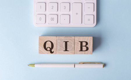 QIB en cubos de madera con pluma y calculadora, concepto financiero