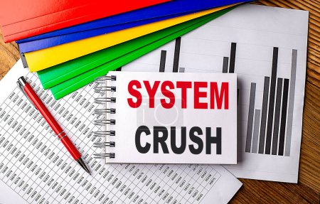 SYSTEM CRUSH text on notebook with pen, folder on a chart background