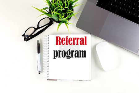 Photo for REFERRAL PROGRAM text written on a notebook with laptop , pen, glasses and mouse , white background - Royalty Free Image