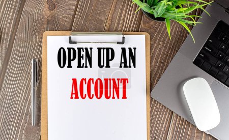 OPEN UP AN ACCOUNT text on a paper clipboard with laptop and mouse on wood background, business concept
