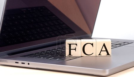 FCA-Wort auf Holzklotz am Laptop, Geschäftskonzept. 