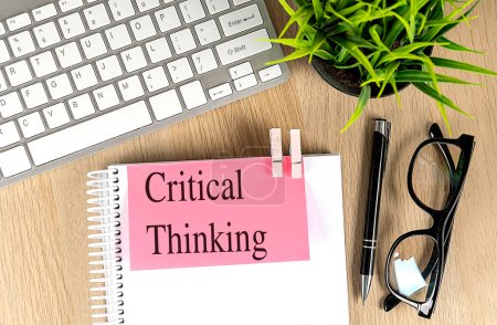 CRITICAL THINKING text pink sticky on a notebook with keyboard, pen and glasses . 