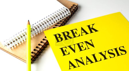 BREAK EVEN ANALYSIS text on a yellow paper with notebooks. 