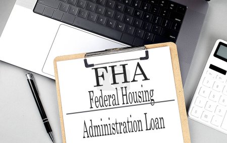 FHA word on clipboard on a laptop with calculator and pen . 