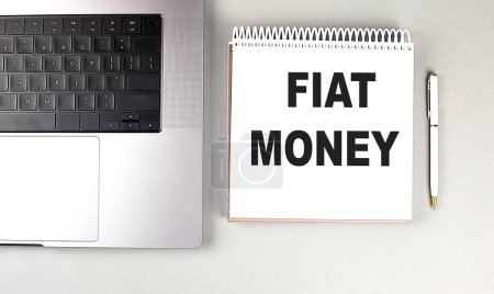 Téléchargez les photos : FIAT MONEY texte sur un carnet avec ordinateur portable et stylo . - en image libre de droit
