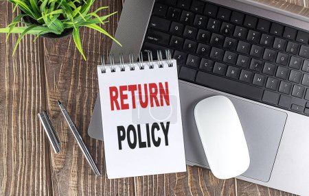 RETURN POLICY text on a notebook with laptop, mouse and pen . 