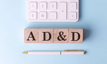 AD and D word on a wooden block with pen and calculator on blue background . 