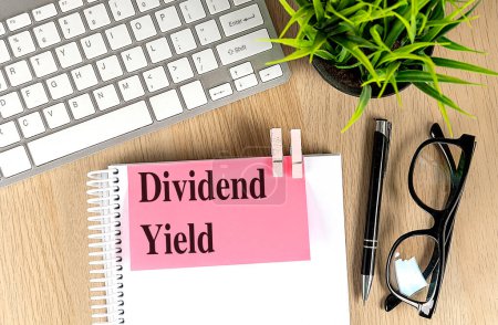 DIVIDEND YIELD text pink sticky on a notebook with keyboard, pen and glasses . 