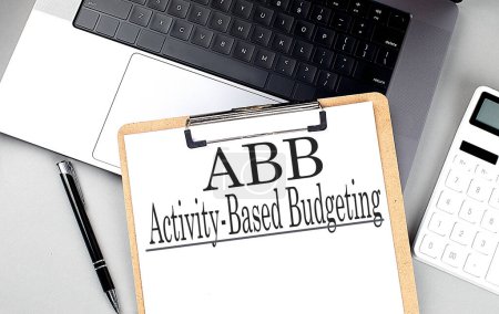 ABB -ACTIVITY BASED HADGETING word auf einer Zwischenablage auf dem Laptop mit Taschenrechner und Stift . 
