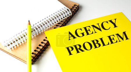 Photo for AGENCY PROBLEM text on a yellow paper with notebooks. - Royalty Free Image