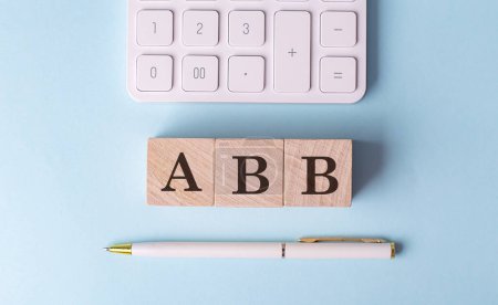 ABB-Wort auf Holzblock mit Stift und Taschenrechner auf blauem Hintergrund . 