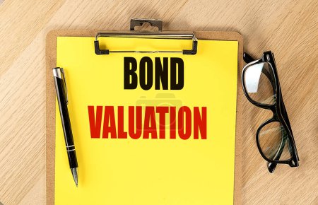 BOND VALUATION text on a yellow paper on clipboard with pen and glasses. 
