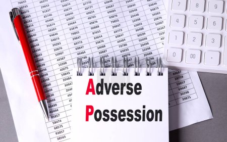 ADVERSE POSSESSION text on a notebook with chart , pen and calculator. 