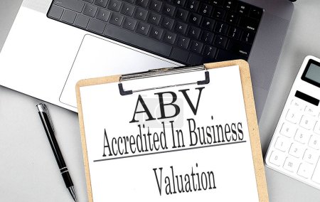 ABV -ACCREDITED IN BUSINESS VALUATION word on a clipboard on laptop with calculator and pen . 