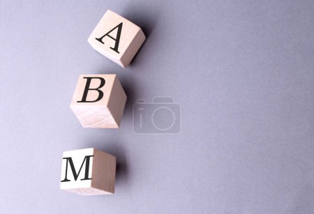 ABM word on a wooden block on gray background 