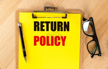 RETURN POLICY text on a yellow paper on clipboard with pen and glasses. 