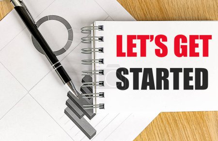 LET'S GET STARTED text on a notebook with chart on wooden background. 