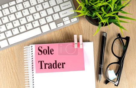 SOLE TRADER text pink sticky on a notebook with keyboard, pen and glasses . 