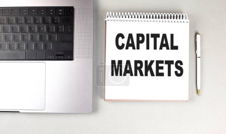 CAPITAL MARKETS text on a notebook with laptop and pen . 
