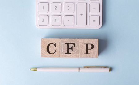 CFP word on a wooden block with pen and calculator on blue background . 