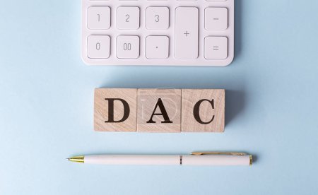 DAC-Wort auf einem Holzblock mit Stift und Taschenrechner auf blauem Hintergrund . 