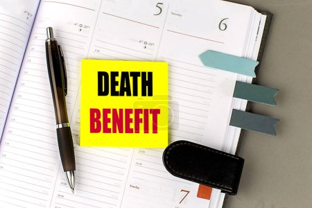 DEATH BENEFIT text sticky on a dairy on gray background. 