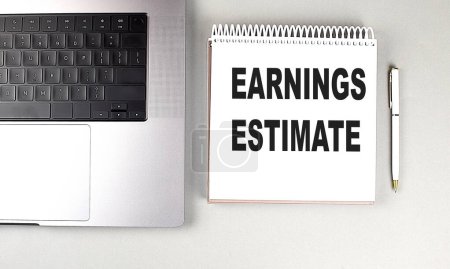 EARNINGS ESTIMATE text on a notebook with laptop and pen . 