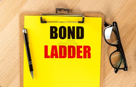 Photo for BOND LADDER text on a yellow paper on clipboard with pen and glasses. - Royalty Free Image