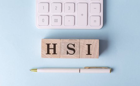 HSI-Wort auf Holzblock mit Stift und Taschenrechner auf blauem Hintergrund .