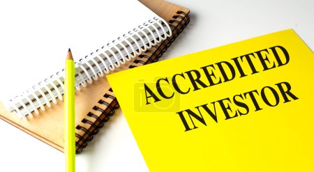 Photo for ACCREDITED INVESTOR text on a yellow paper with notebooks. - Royalty Free Image