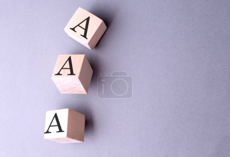 AAA-Wort auf einem Holzblock auf grauem Hintergrund 