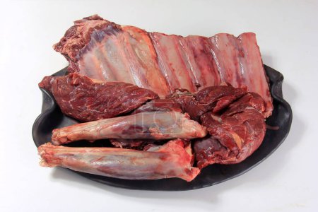 Roh-Hirschfilet, Rippen und Beine auf schwarzem Teller, weißer Hintergrund, Rehfleisch