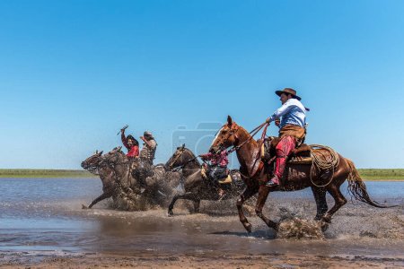 Photo for Esquina, Corrientes, Argentina - October 29, 2022: Side view of five Argentine gauchos riding their horses across the river - Royalty Free Image