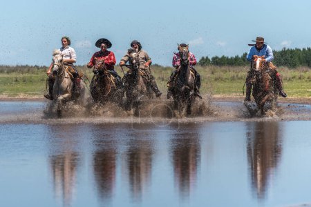 Foto de Esquina, Corrientes, Argentina - 29 de octubre de 2022: Vista frontal de cinco gauchos argentinos cabalgando sus caballos a través del río - Imagen libre de derechos