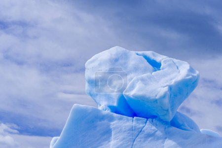 A large piece of ice is sitting on top of an iceberg hill. The sky is cloudy and the sun is not visible. Scene is calm and serene.