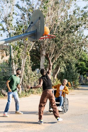 Latin man en fauteuil roulant jouant au baskteball avec des amis afro-américains et hispaniques