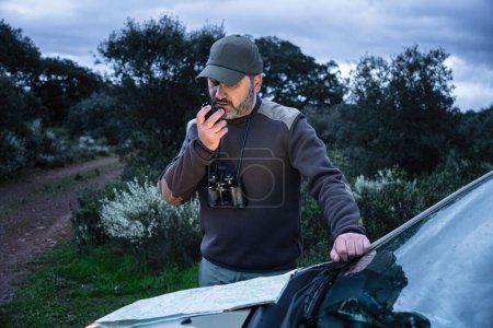 Forester Rural Ranger talking on walkie talkie radio checking road map at night - Environmental Wildlife Conservation Job