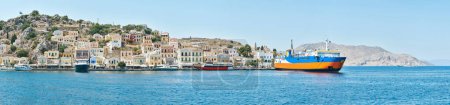Bunte Häuser auf den Hügeln der Insel Symi vom Wasser aus gesehen. Küstenstadt an der türkisfarbenen Küste Griechenlands. Touristenschiffe legen direkt am Meer an
