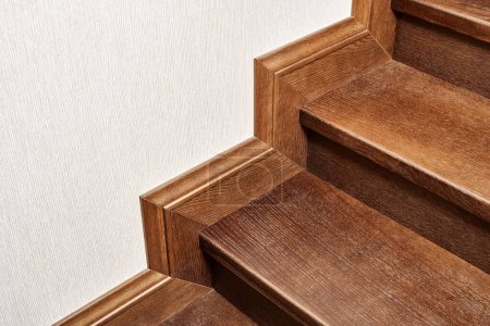 Wooden steps of indoor staircase with stair skirtboard made of toned solid oak and oak veneer close view