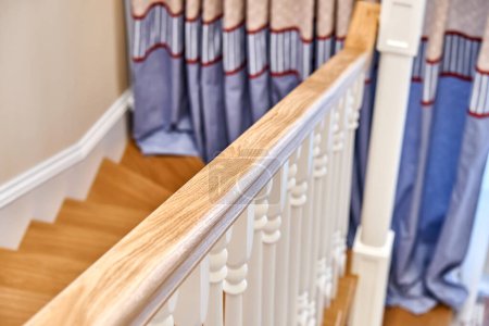Pasamanos de madera de roble macizo con balaustres blancos. Escalera de madera de estilo clásico en una habitación grande y luminosa