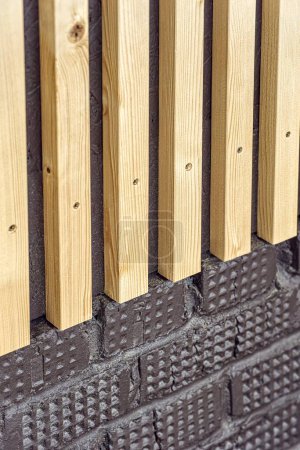 Building wall decorated with stylish wooden slats made of thin light planks on house terrace extreme close view
