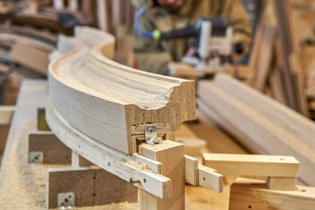 Barandilla de escalera de madera curvada hecha de tablones de roble y madera contrachapada en primer plano de la mesa. Detalle de valla de escaleras en taller de carpintería