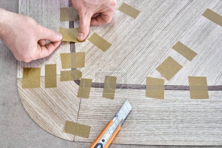 Tischler fugt Furnier mit Klebeband für Tischplatte des Esstisches mit geometrischem Muster auf Werkbank in Werkstattansicht oben schließen