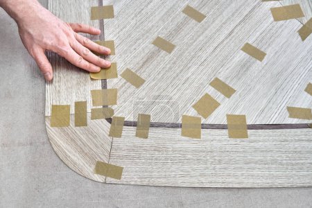 Tischler fugt Furnier mit Klebeband für Tischplatte des Esstisches mit geometrischem Muster auf Werkbank in Werkstattansicht oben schließen