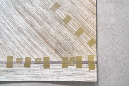 Fugenfurnier mit Klebeband in Leinwand für Tischplatte des Esstisches mit geometrischem Muster auf Werkbank in Werkstattansicht oben schließen