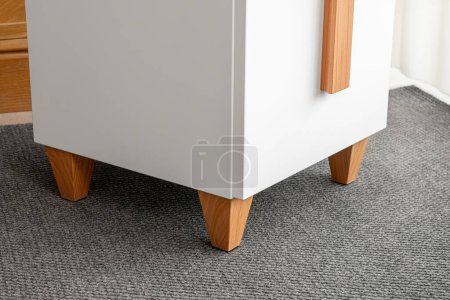 Minimalist white office chest of drawers with natural wooden brown handles and legs closeup view. Stylish furniture model