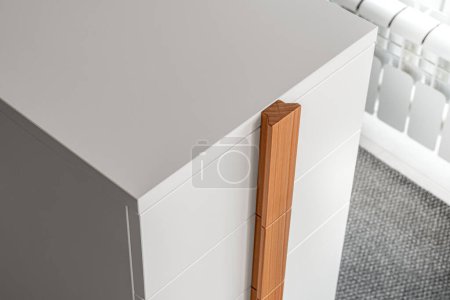 Minimalist white office chest of drawers with natural wooden brown handles and legs closeup view. Stylish furniture model