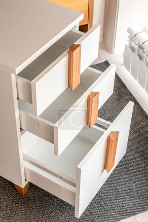 Stylish white office commode with wooden handles and legs with open empty drawers closeup view. Comfortable furniture for home and office furnishing